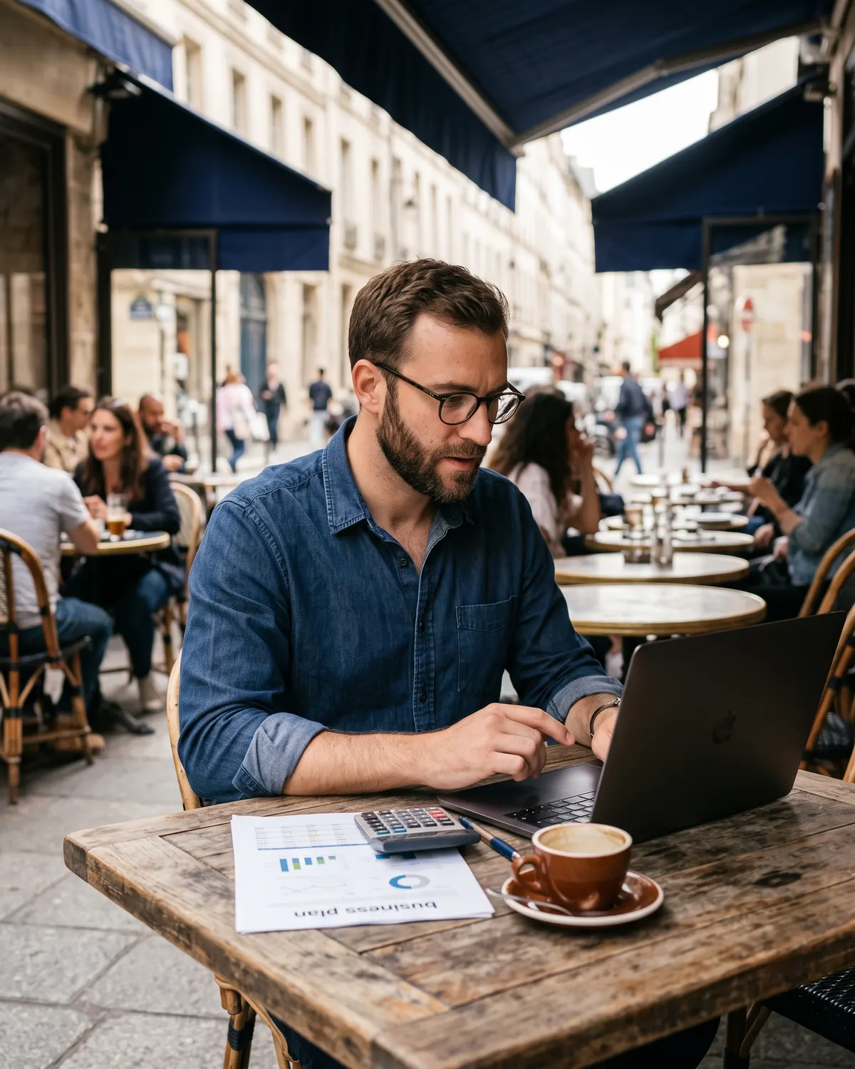 Un porteur de projet travaille son prévisionnel financier sur ordinateur à la terrasse d’un café